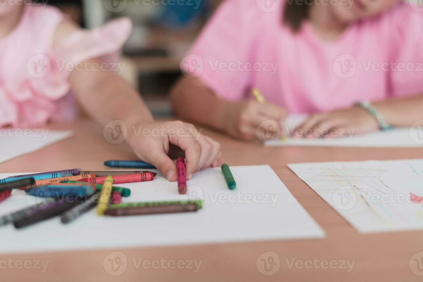 Little girls sitting in elementary school drawing on paper with their friends while sitting in a modern classroom photo