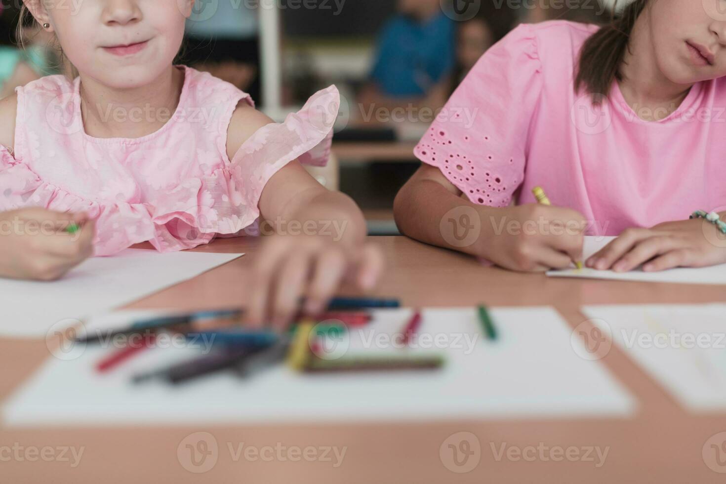 Little girls sitting in elementary school drawing on paper with their friends while sitting in a modern classroom photo
