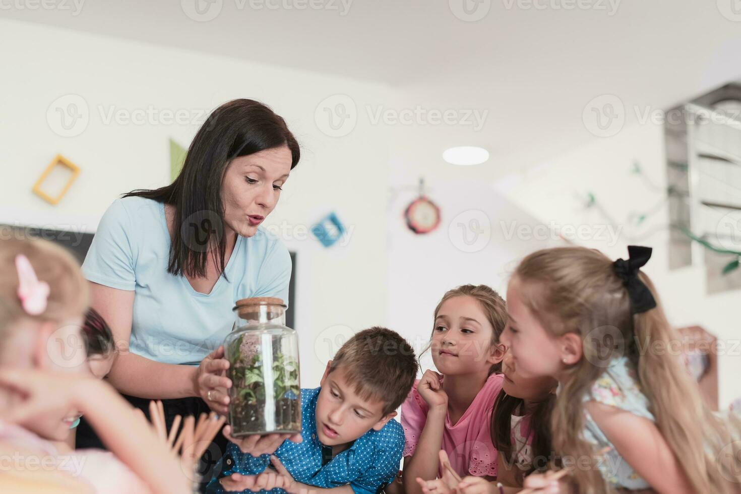 Female Teacher with kids in biology class at elementary school conducting biology or botanical scientific experiment about sustainable Growing plants. Learning about plants in a glass jar photo