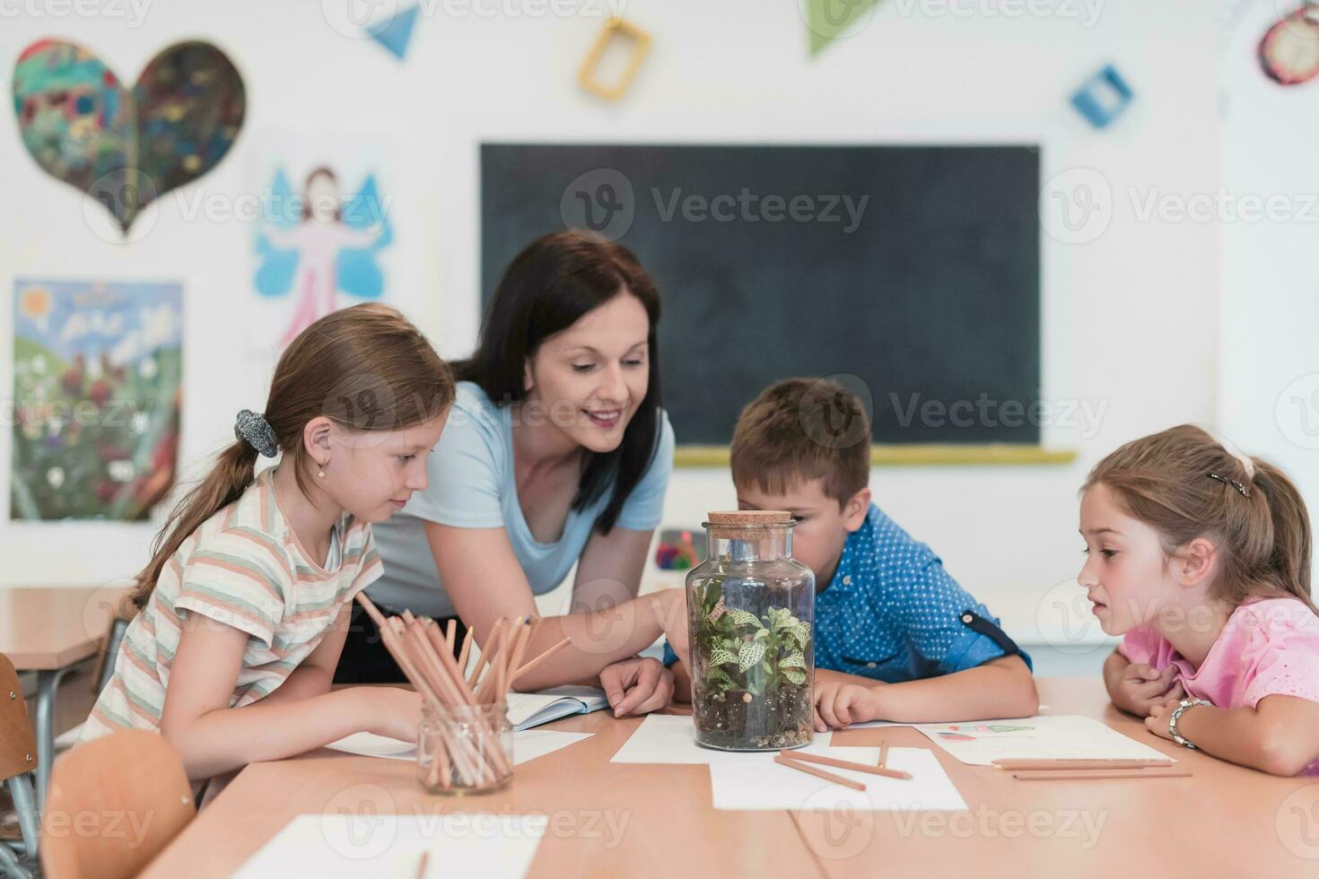 Female Teacher with kids in biology class at elementary school conducting biology or botanical scientific experiment about sustainable Growing plants. Learning about plants in a glass jar photo