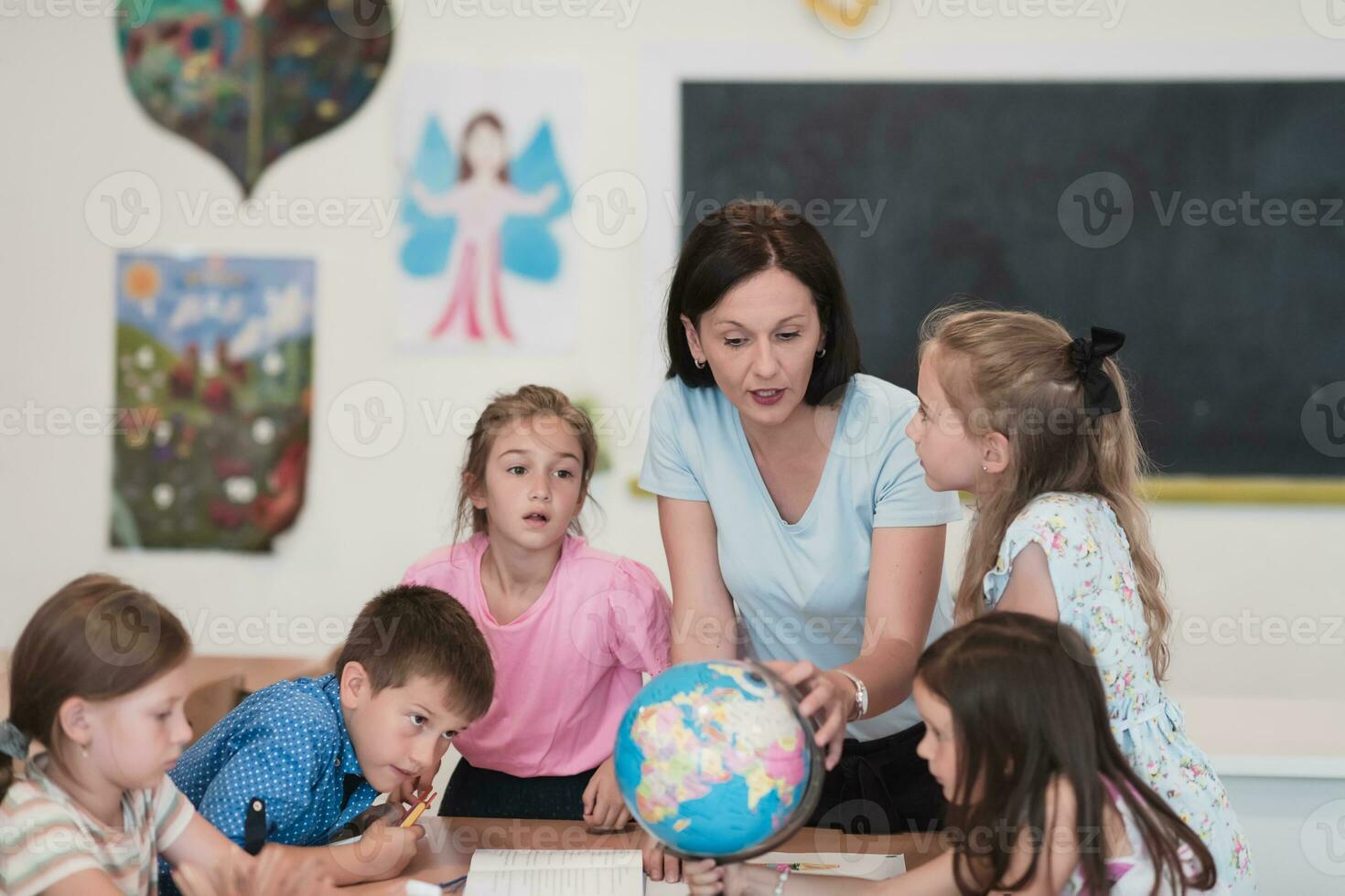 Female teacher with kids in geography class looking at globe. Side view of group of diverse happy school kids with globe in classroom at school. photo