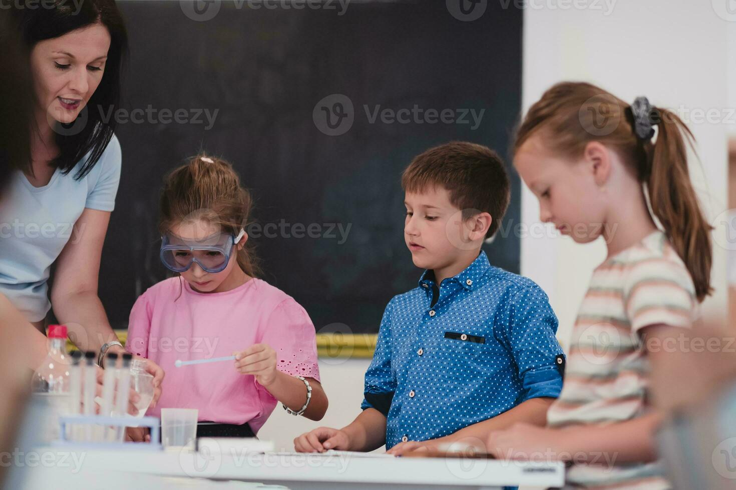 Elementary School Science Classroom Enthusiastic Teacher Explains Chemistry to Diverse Group of Children, Little Boy Mixes Chemicals in Beakers. Children Learn with Interest photo