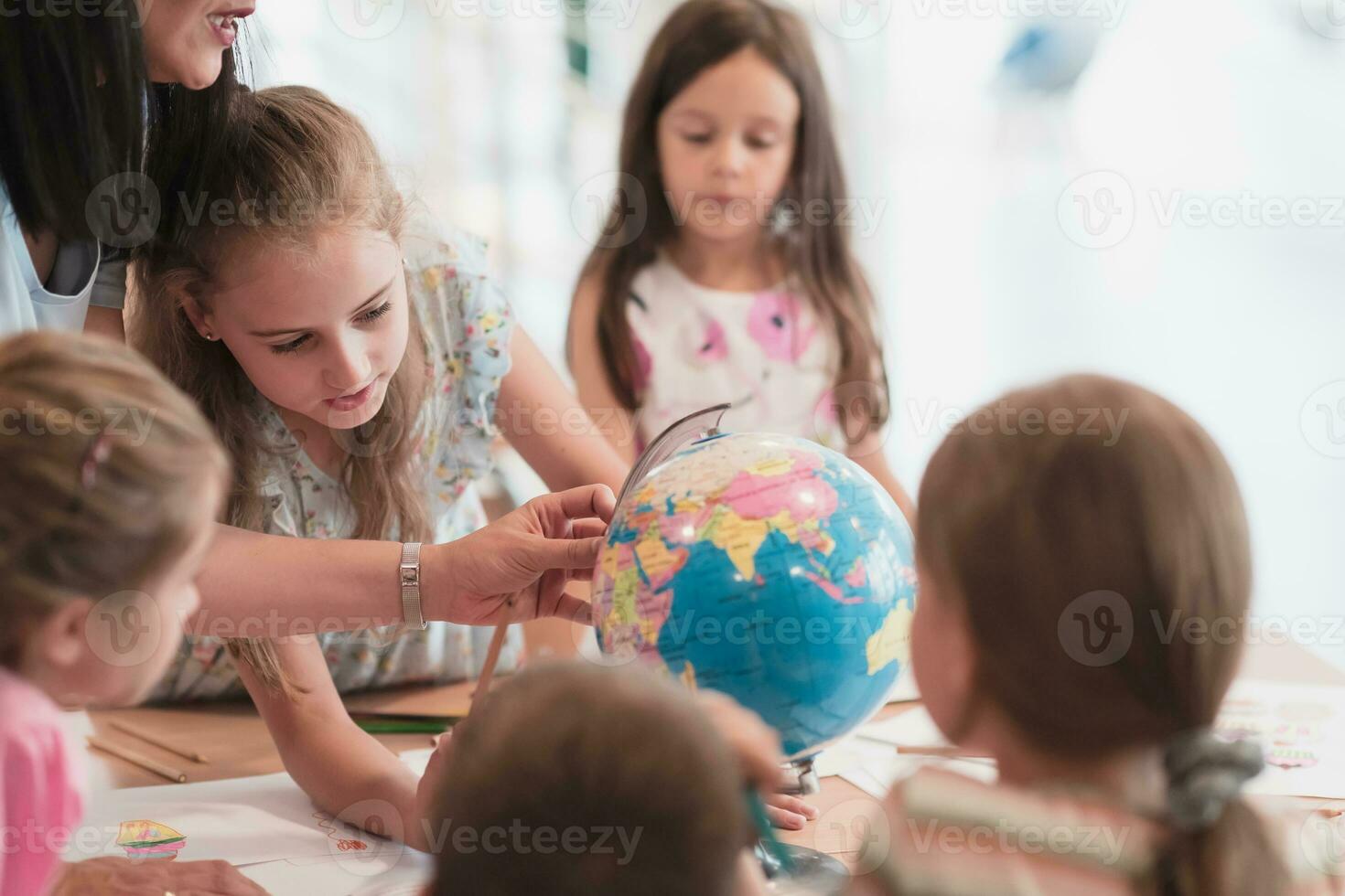 Female teacher with kids in geography class looking at globe. Side view of group of diverse happy school kids with globe in classroom at school. photo