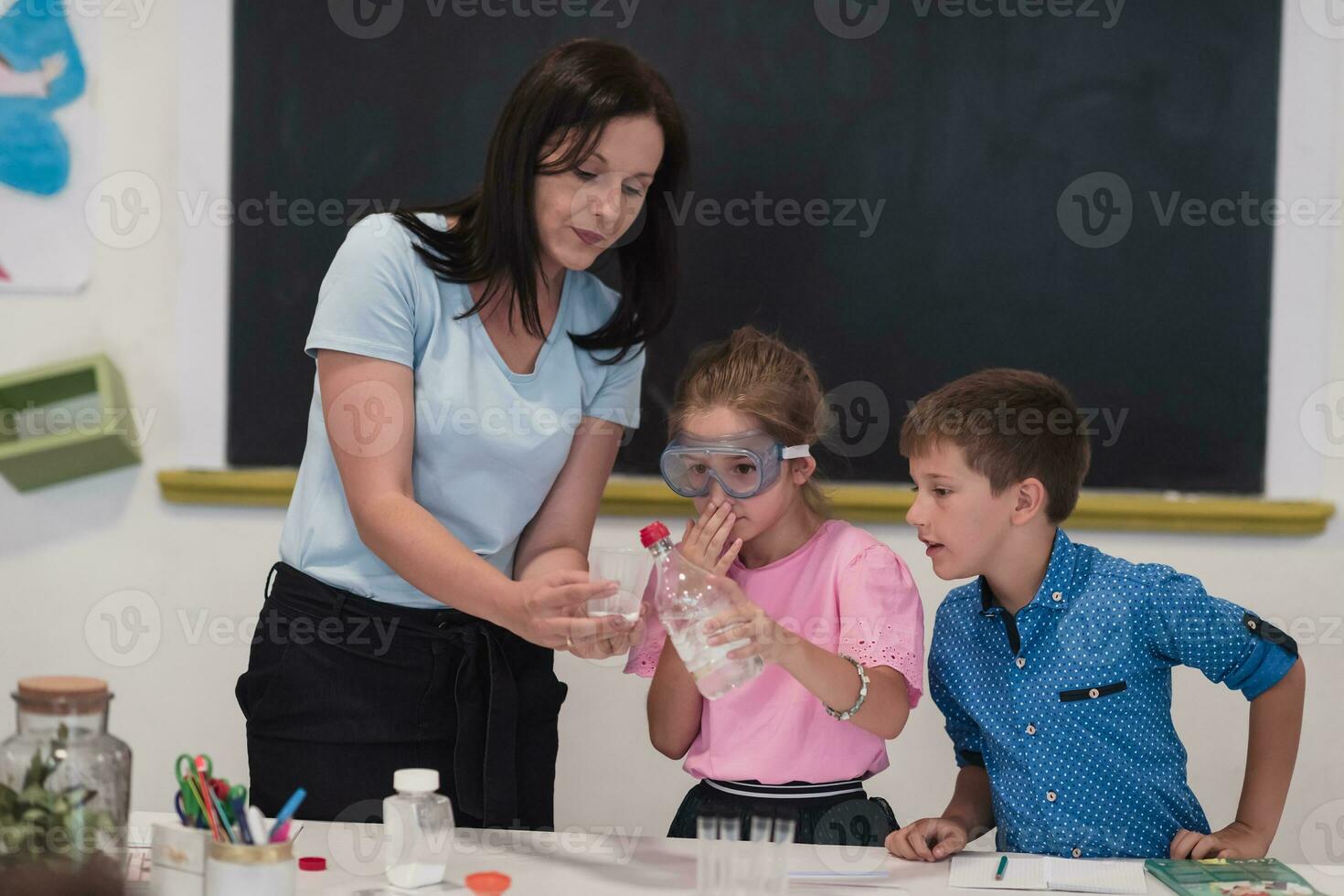 Elementary School Science Classroom Enthusiastic Teacher Explains Chemistry to Diverse Group of Children, Little Boy Mixes Chemicals in Beakers. Children Learn with Interest photo