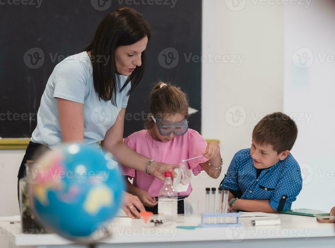 Elementary School Science Classroom Enthusiastic Teacher Explains Chemistry to Diverse Group of Children, Little Boy Mixes Chemicals in Beakers. Children Learn with Interest photo