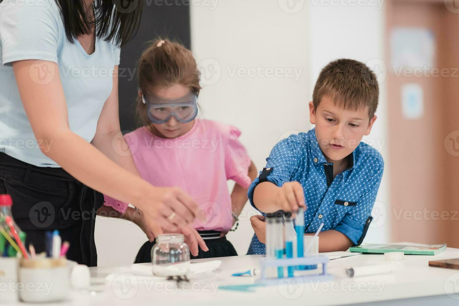 Elementary School Science Classroom Enthusiastic Teacher Explains Chemistry to Diverse Group of Children, Little Boy Mixes Chemicals in Beakers. Children Learn with Interest photo