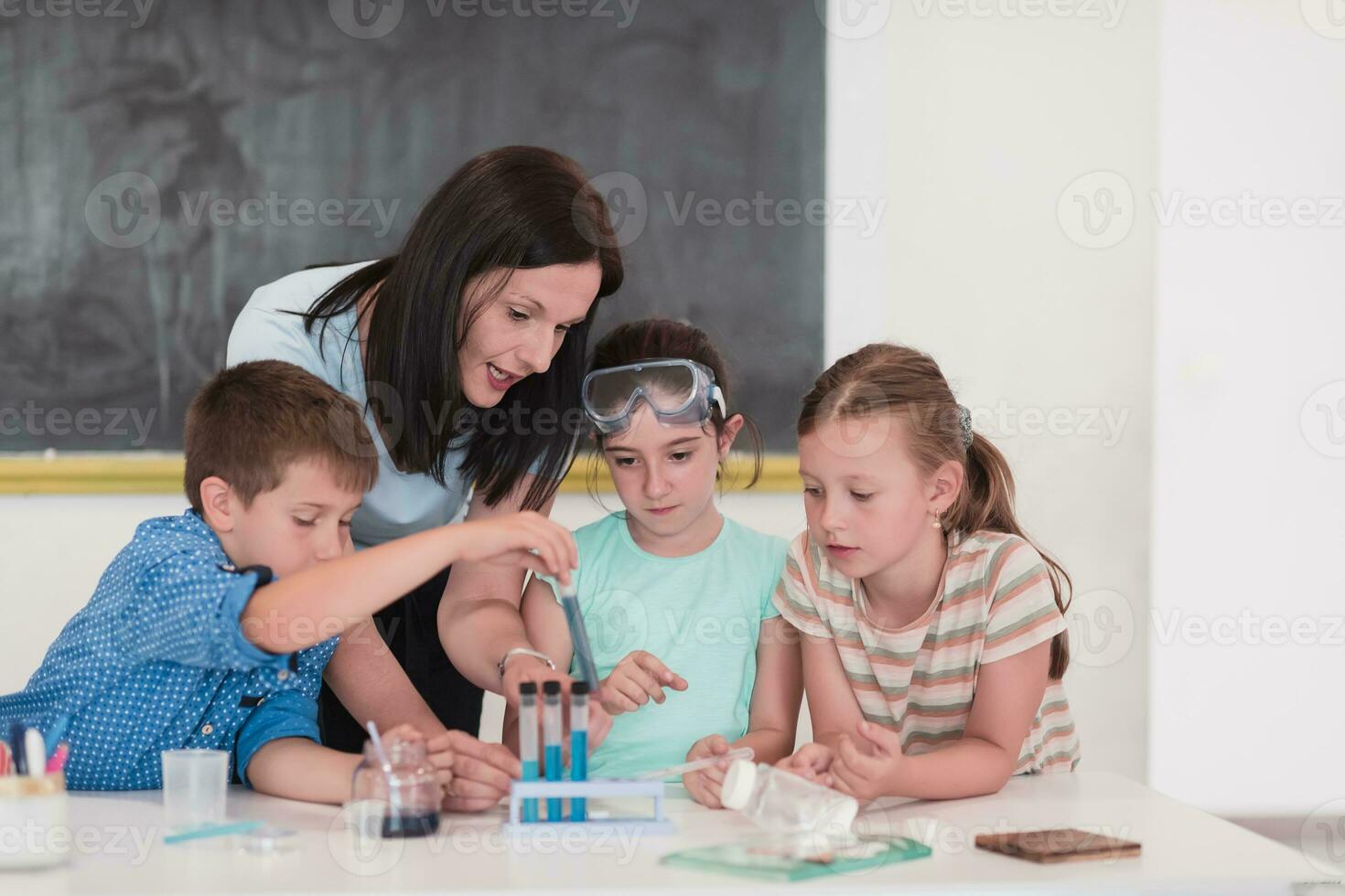 Elementary School Science Classroom Enthusiastic Teacher Explains Chemistry to Diverse Group of Children, Little Boy Mixes Chemicals in Beakers. Children Learn with Interest photo