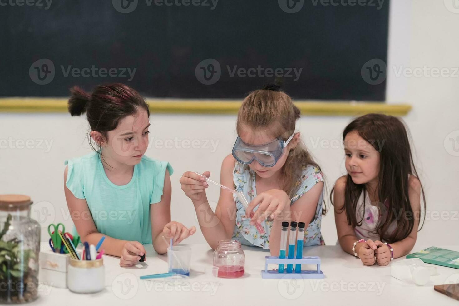 Elementary School Science Classroom Enthusiastic Teacher Explains Chemistry to Diverse Group of Children, Little Boy Mixes Chemicals in Beakers. Children Learn with Interest photo