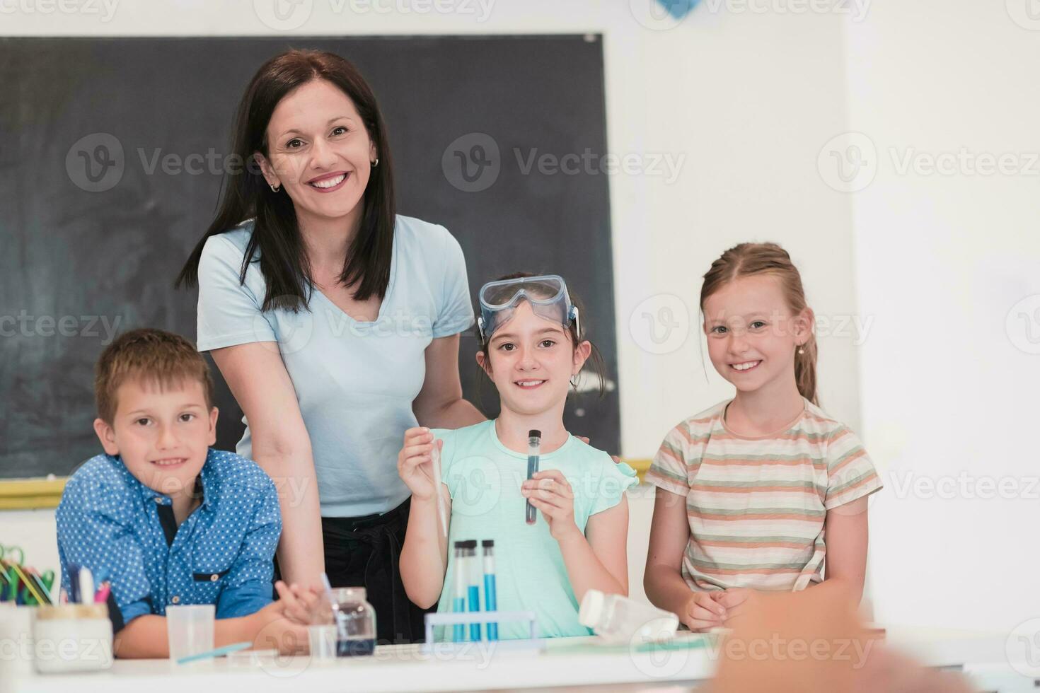 Elementary School Science Classroom Enthusiastic Teacher Explains Chemistry to Diverse Group of Children, Little Boy Mixes Chemicals in Beakers. Children Learn with Interest photo