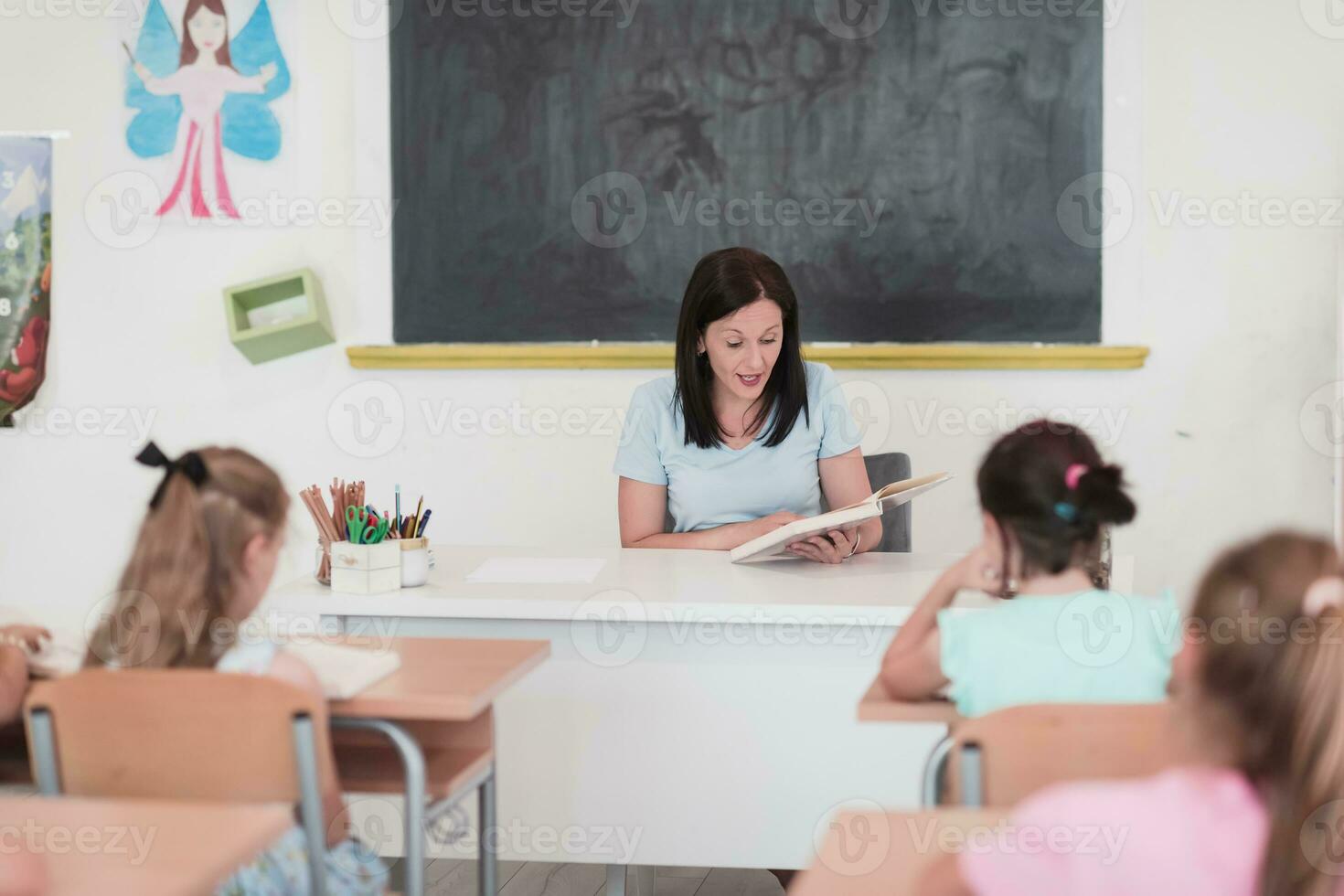 un profesor lee un libro a elemental colegio estudiantes quien escucha cuidadosamente mientras sentado en un moderno salón de clases foto