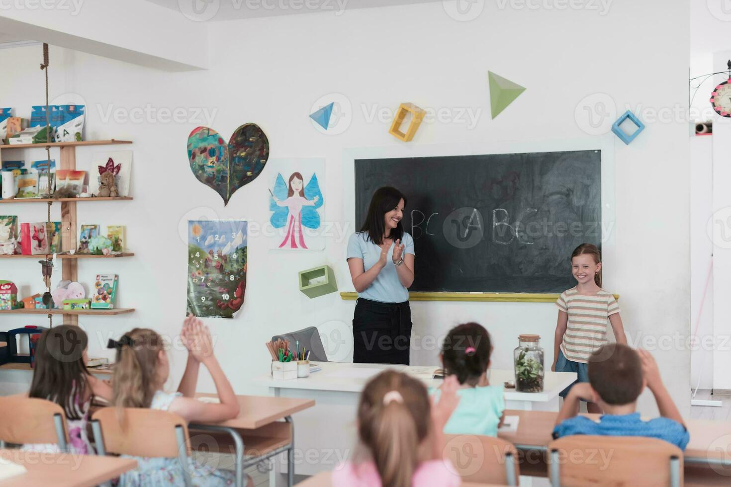 Elementary school. The female teacher helping the child student while writing the answer on the chalkboard. photo