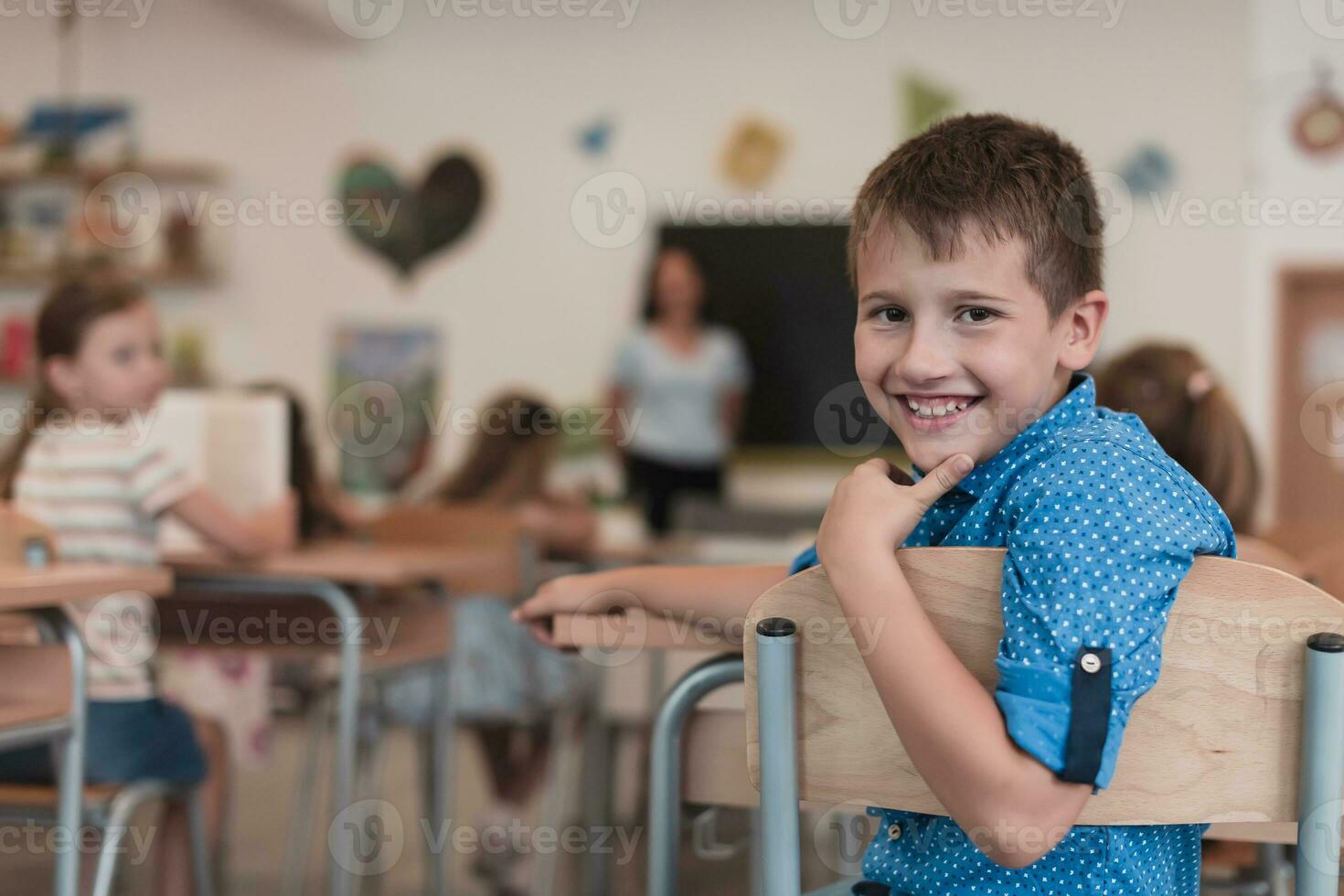 Little boy sitting in elementary school drawing on paper with their friends while sitting in a modern classroom photo