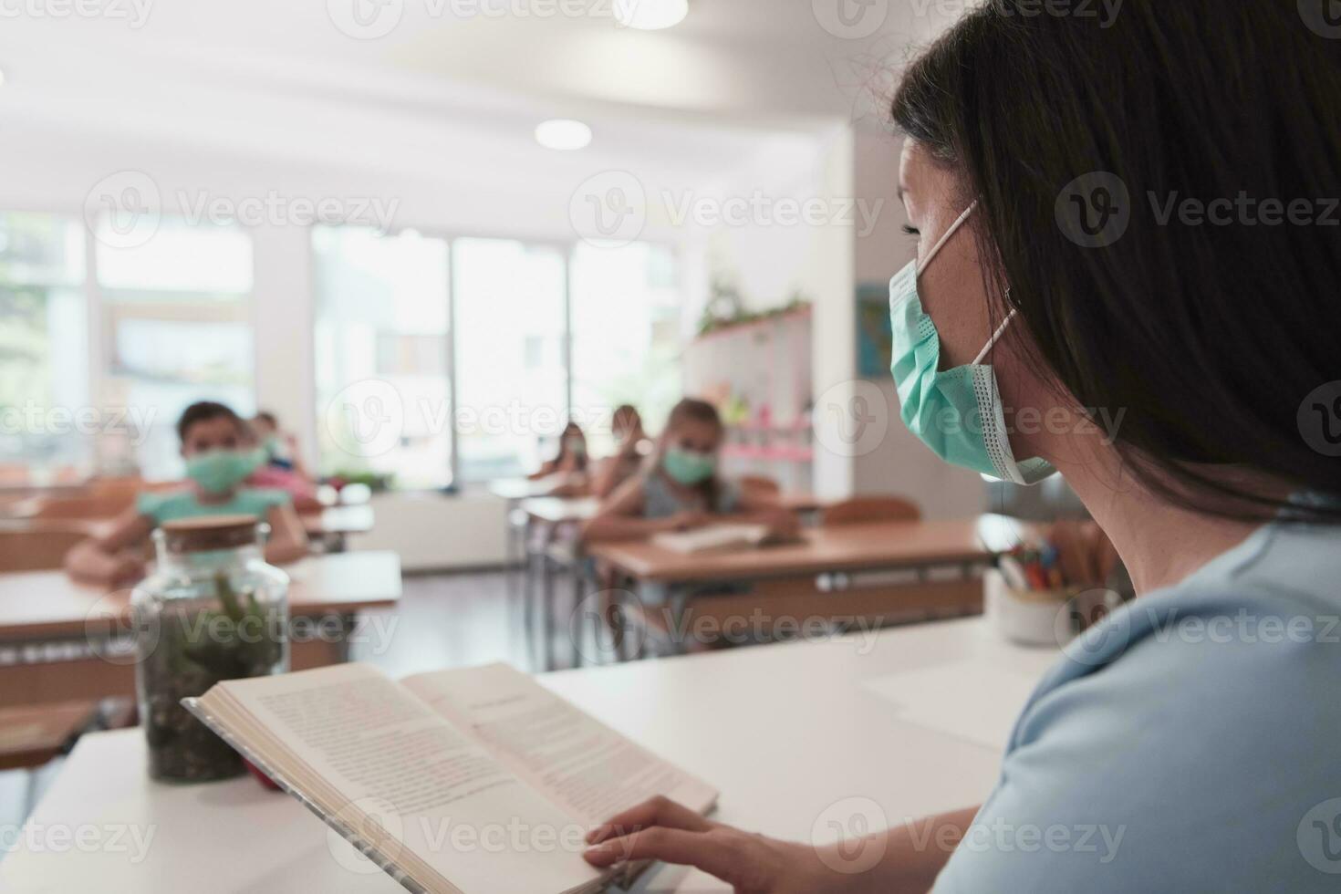 Multiracial group of kids wearing face masks working at class, writing and listening explanations of teacher in classroom photo