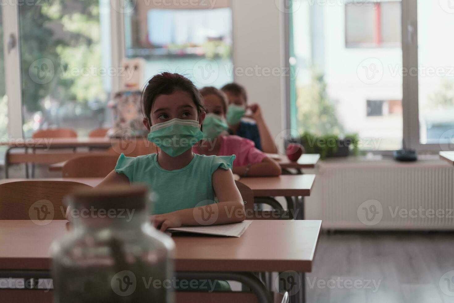 Multiracial group of kids wearing face masks working at class, writing and listening explanations of teacher in classroom photo