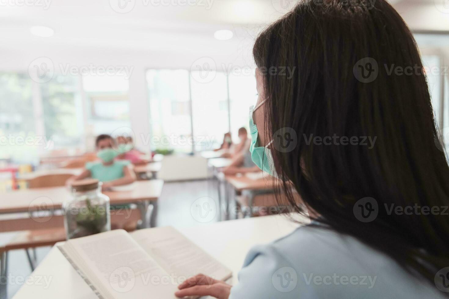 Multiracial group of kids wearing face masks working at class, writing and listening explanations of teacher in classroom photo