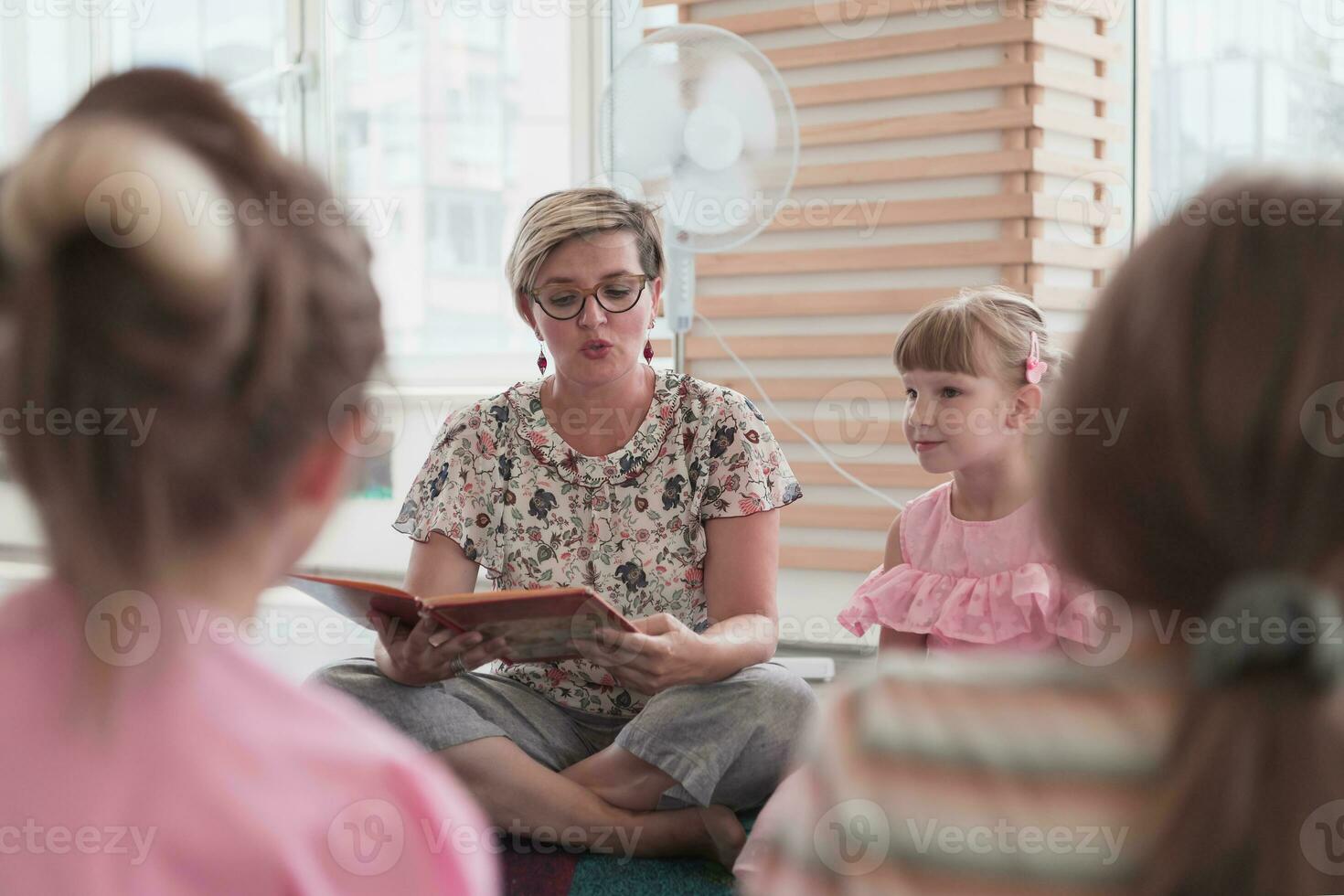 Reading time in elementary school or kindergarten, teacher reading a book to kids in elementary school or kindergaden. Selective focus photo