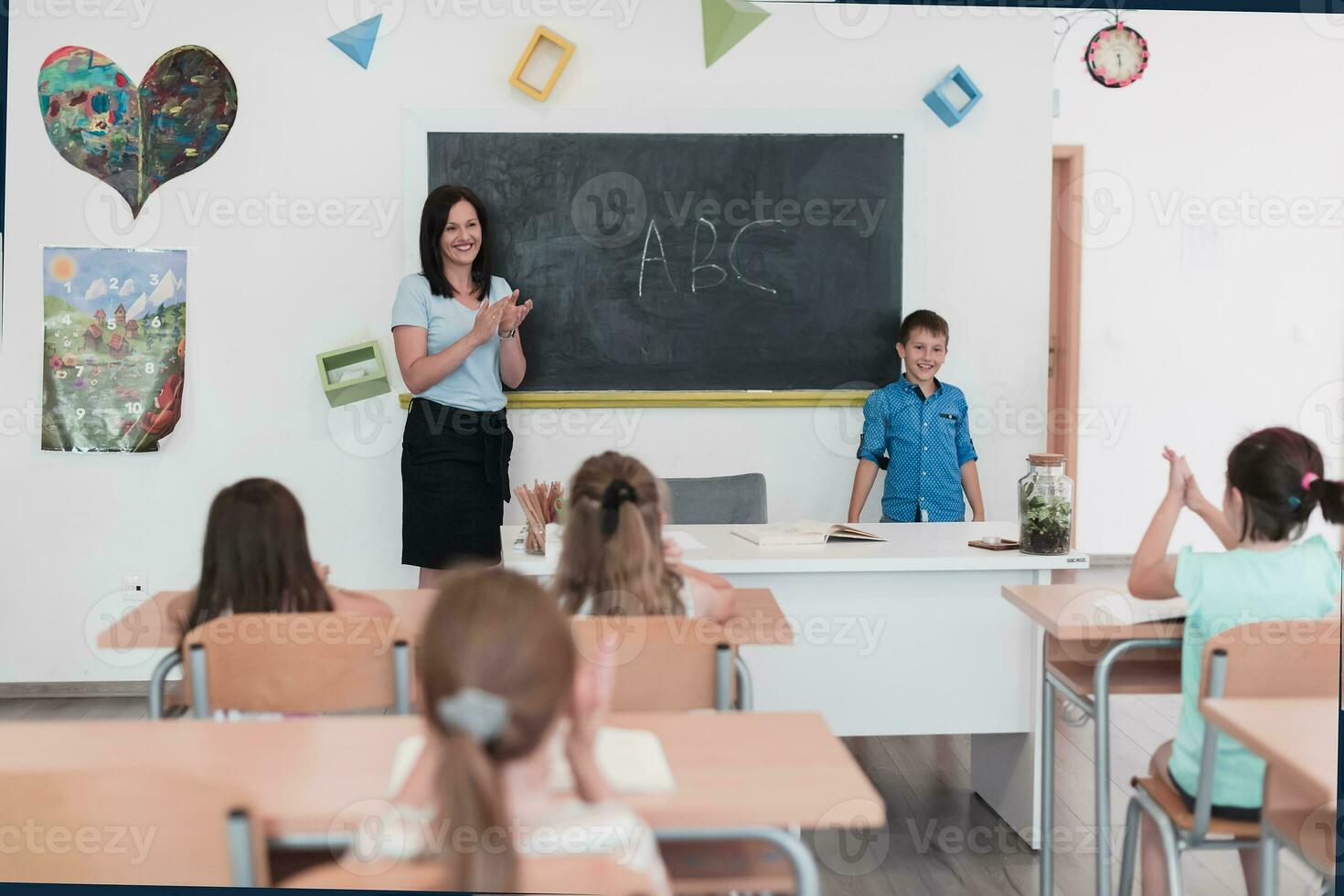 Elementary school. The female teacher helping the child student while writing the answer on the chalkboard. photo