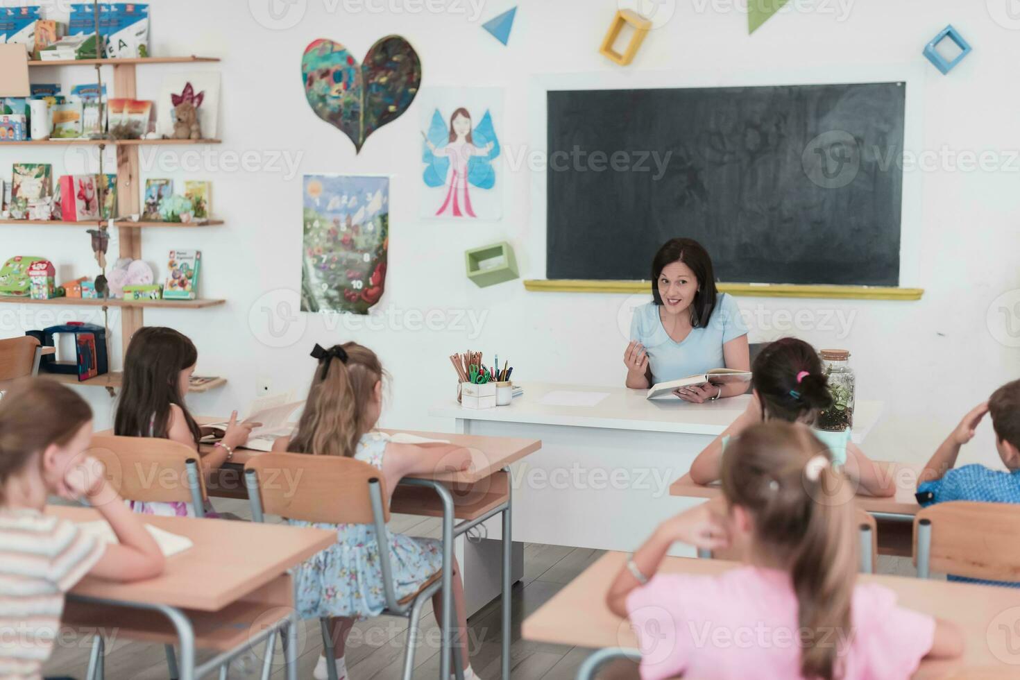 un profesor lee un libro a elemental colegio estudiantes quien escucha cuidadosamente mientras sentado en un moderno salón de clases foto