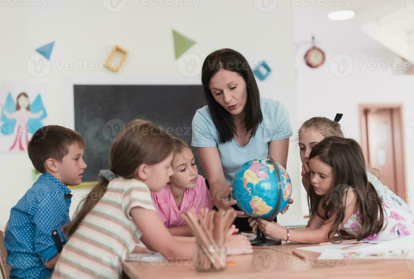 Female teacher with kids in geography class looking at globe. Side view of group of diverse happy school kids with globe in classroom at school. photo