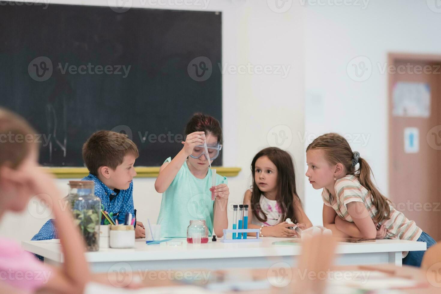 Elementary School Science Classroom Enthusiastic Teacher Explains Chemistry to Diverse Group of Children, Little Boy Mixes Chemicals in Beakers. Children Learn with Interest photo