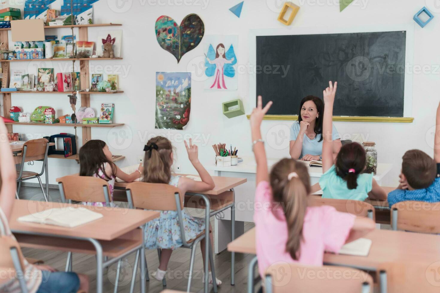 Elementary school. The female teacher helping the child student while writing the answer on the chalkboard. photo