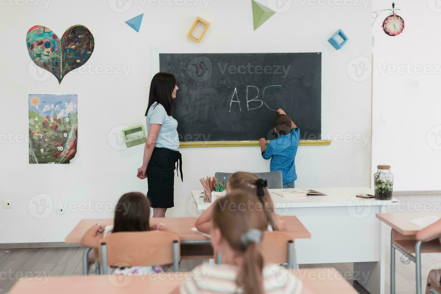 elemental escuela. el hembra profesor Ayudar el niño estudiante mientras escritura el responder en el pizarra foto