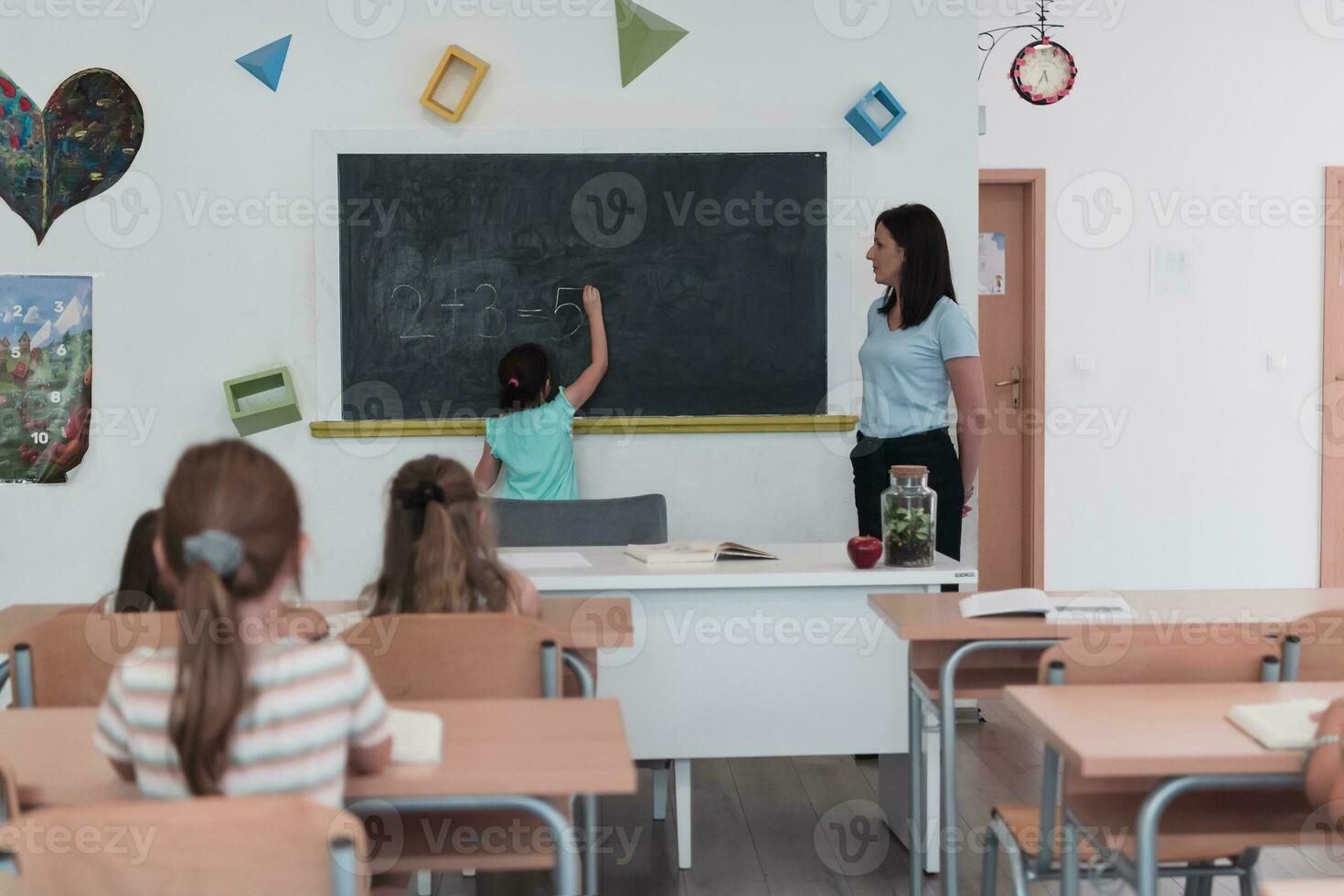 Elementary school. The female teacher helping the child student while writing the answer on the chalkboard. photo