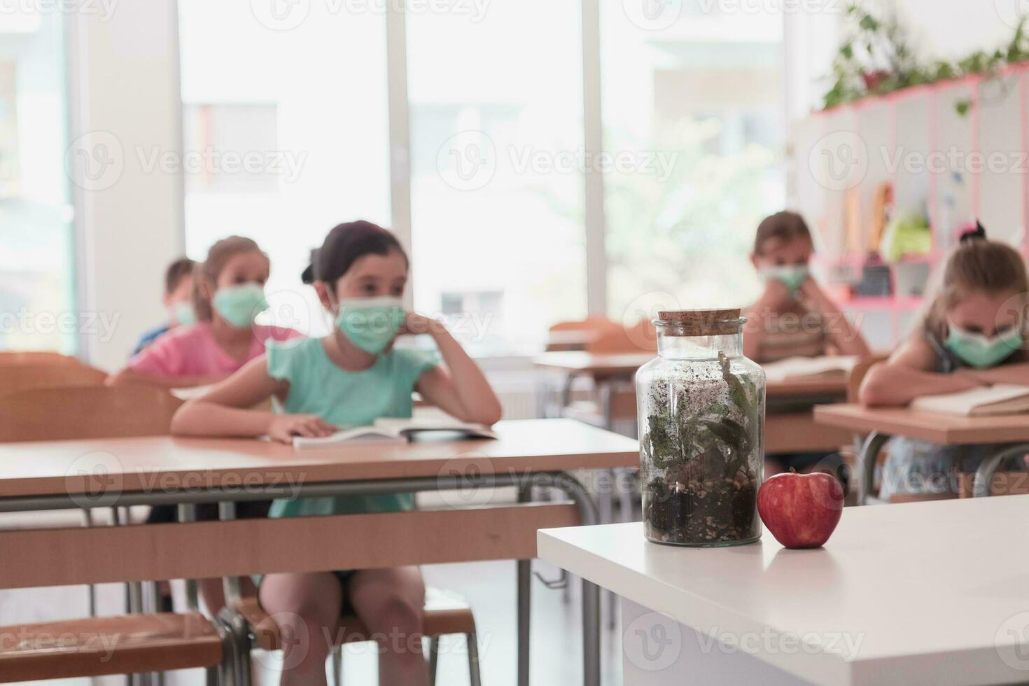 Multiracial group of kids wearing face masks working at class, writing and listening explanations of teacher in classroom photo