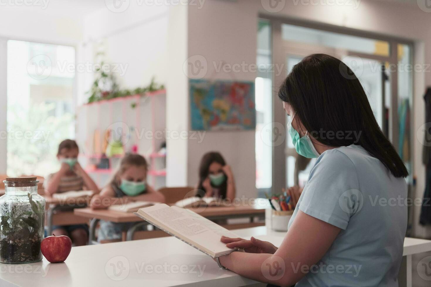 Multiracial group of kids wearing face masks working at class, writing and listening explanations of teacher in classroom photo