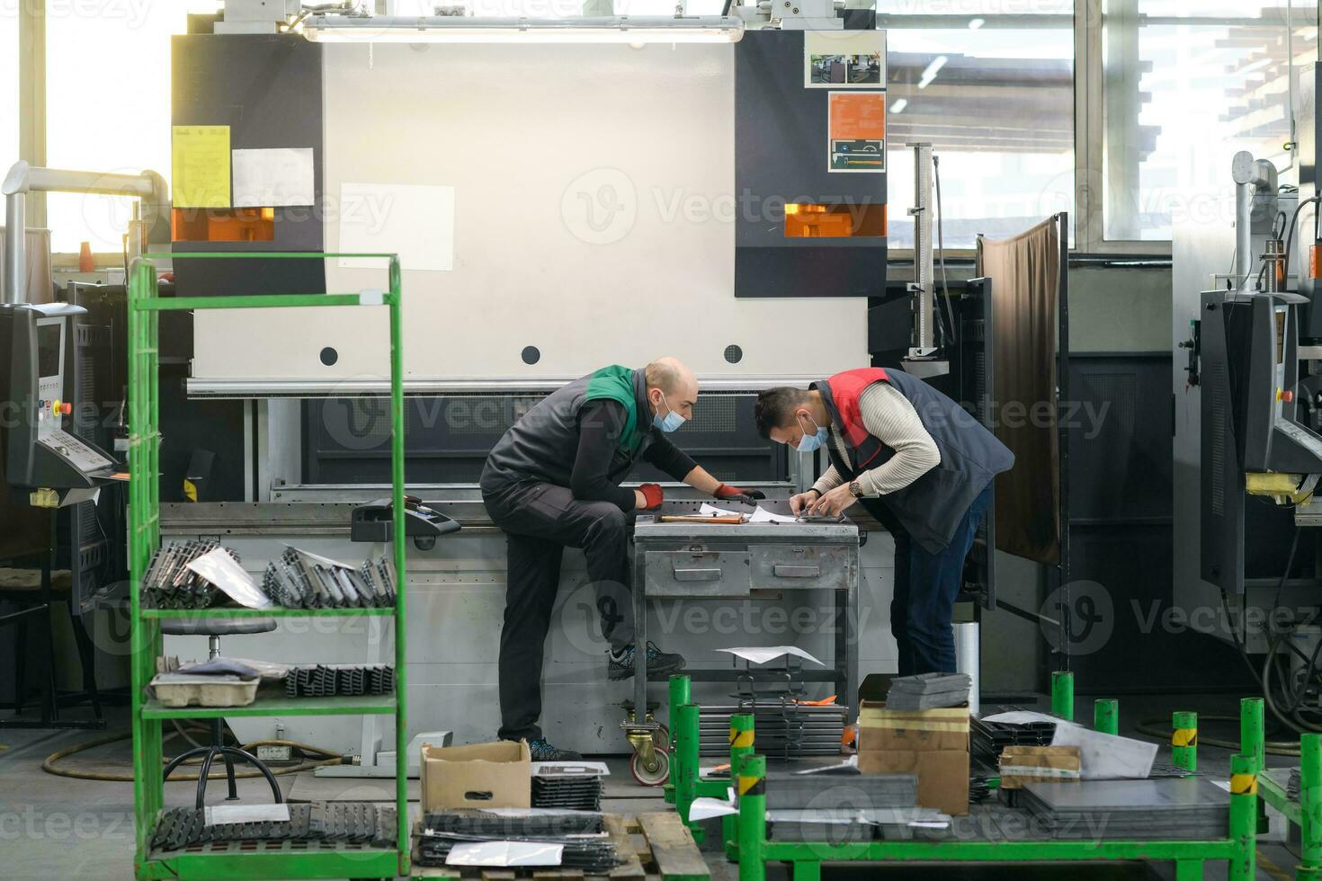 two workers wearing a protective mask due to a coronavirus pandemic, working in a modern factory and preparing a program for a cnc machine photo