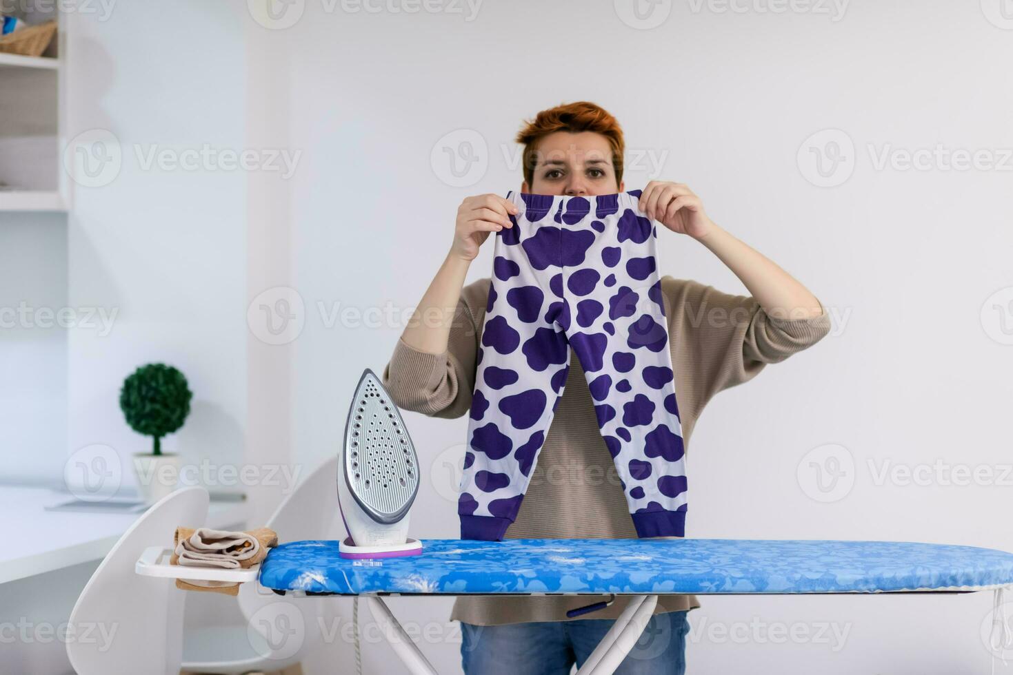 Red haired woman ironing clothes at home photo