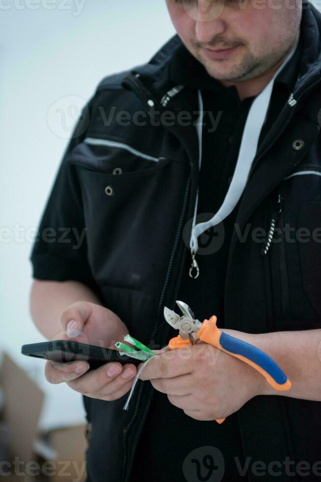 electrical engineer with wire and pliers in his hand using mobile phone photo