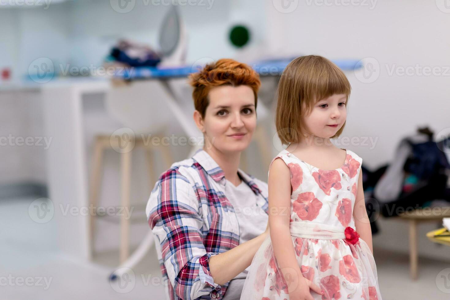 mother helping daughter while putting on a dress photo