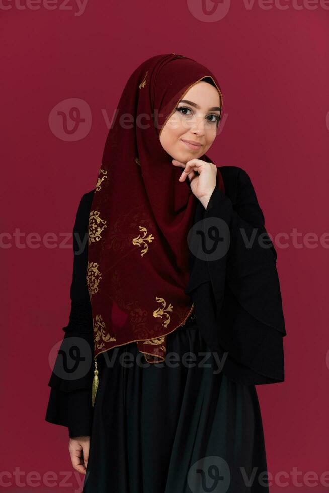beautiful muslim woman in fashinable dress with hijab isolated on modern red background representing concept of modern islam and ramadan kareem photo