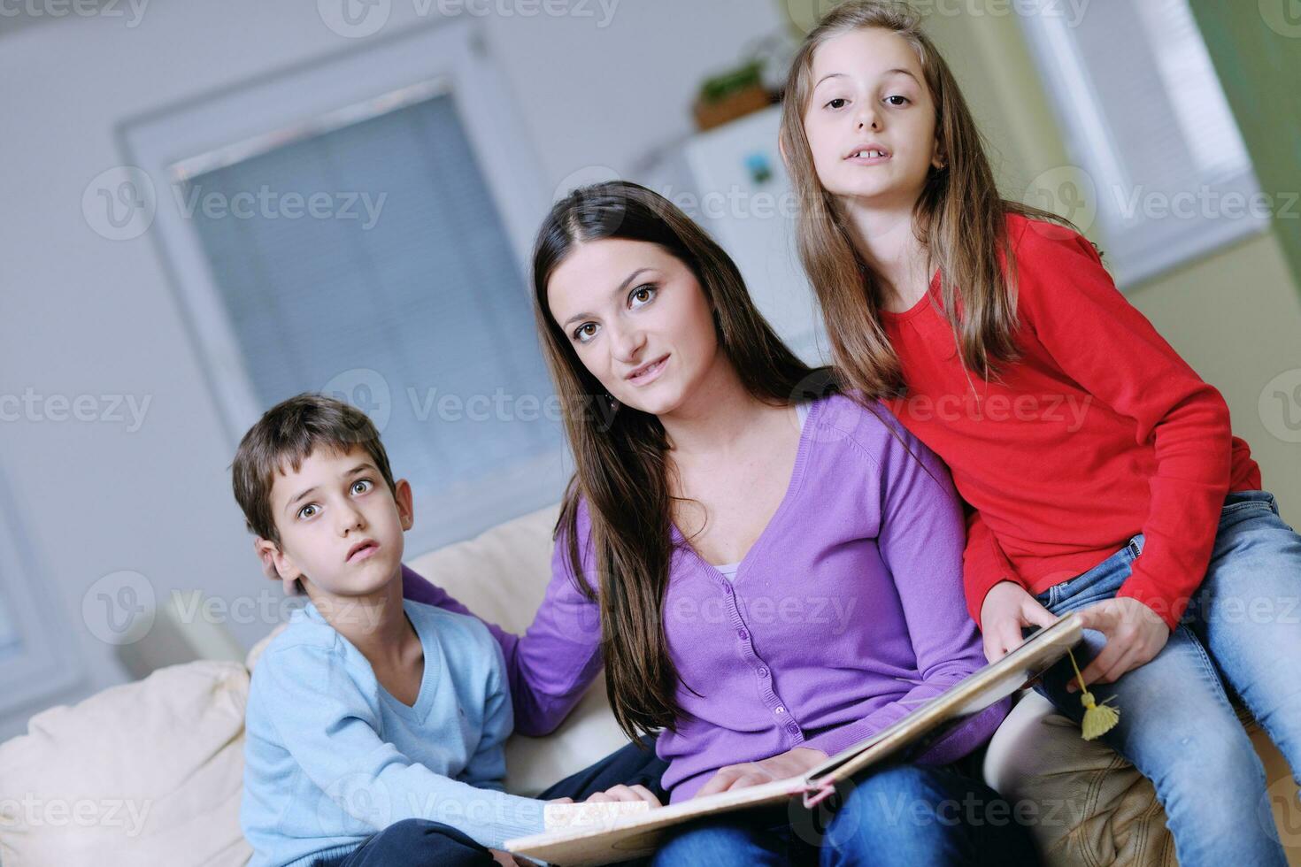 mamá joven juega con sus hijos en casa y lee libros foto