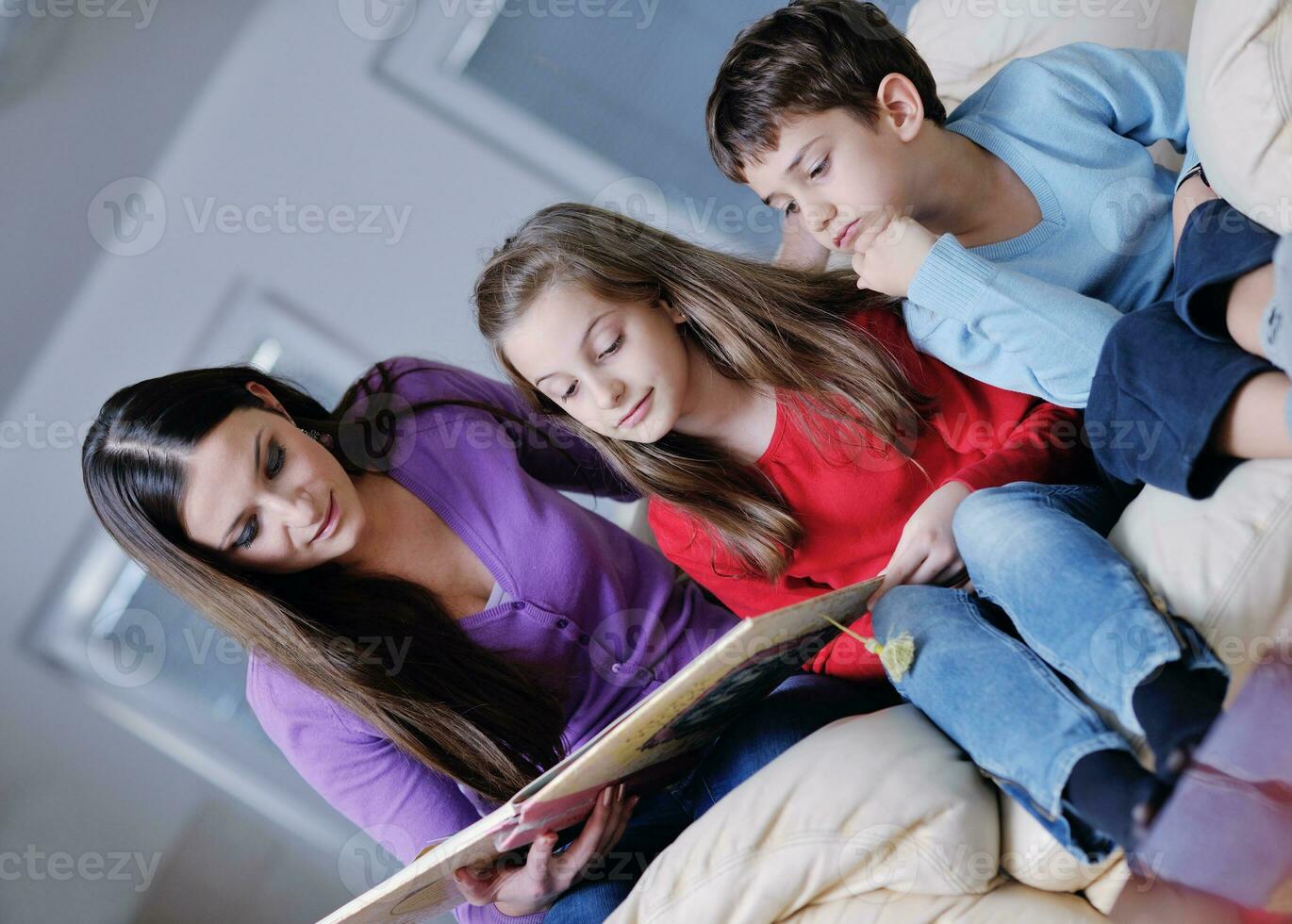 mamá joven juega con sus hijos en casa y lee libros foto