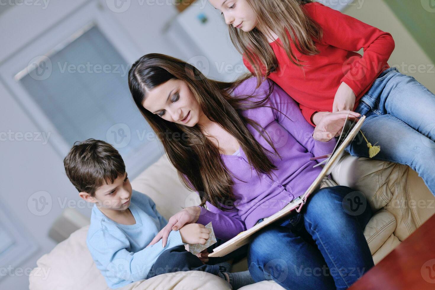 mamá joven juega con sus hijos en casa y lee libros foto