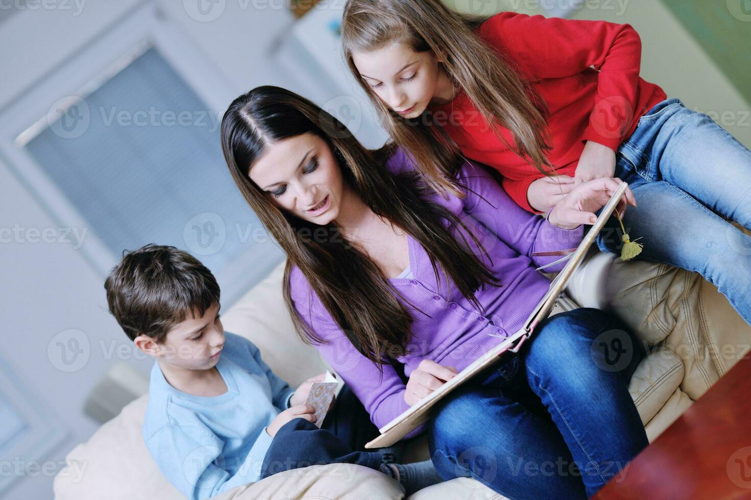 mamá joven juega con sus hijos en casa y lee libros foto