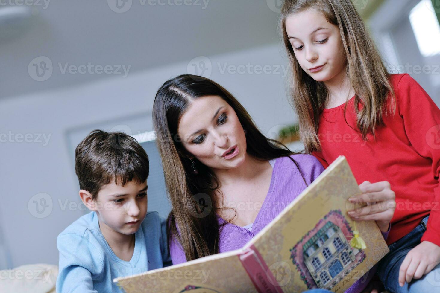 mamá joven juega con sus hijos en casa y lee libros foto