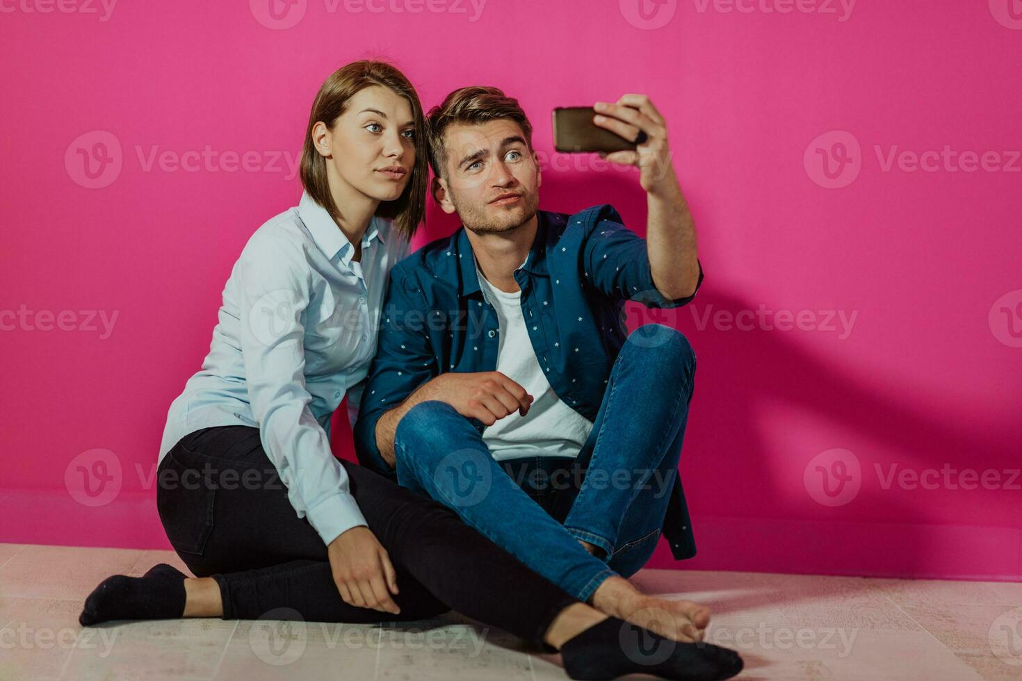 A happy young couple sitting on the floor in the house and making selfie photo