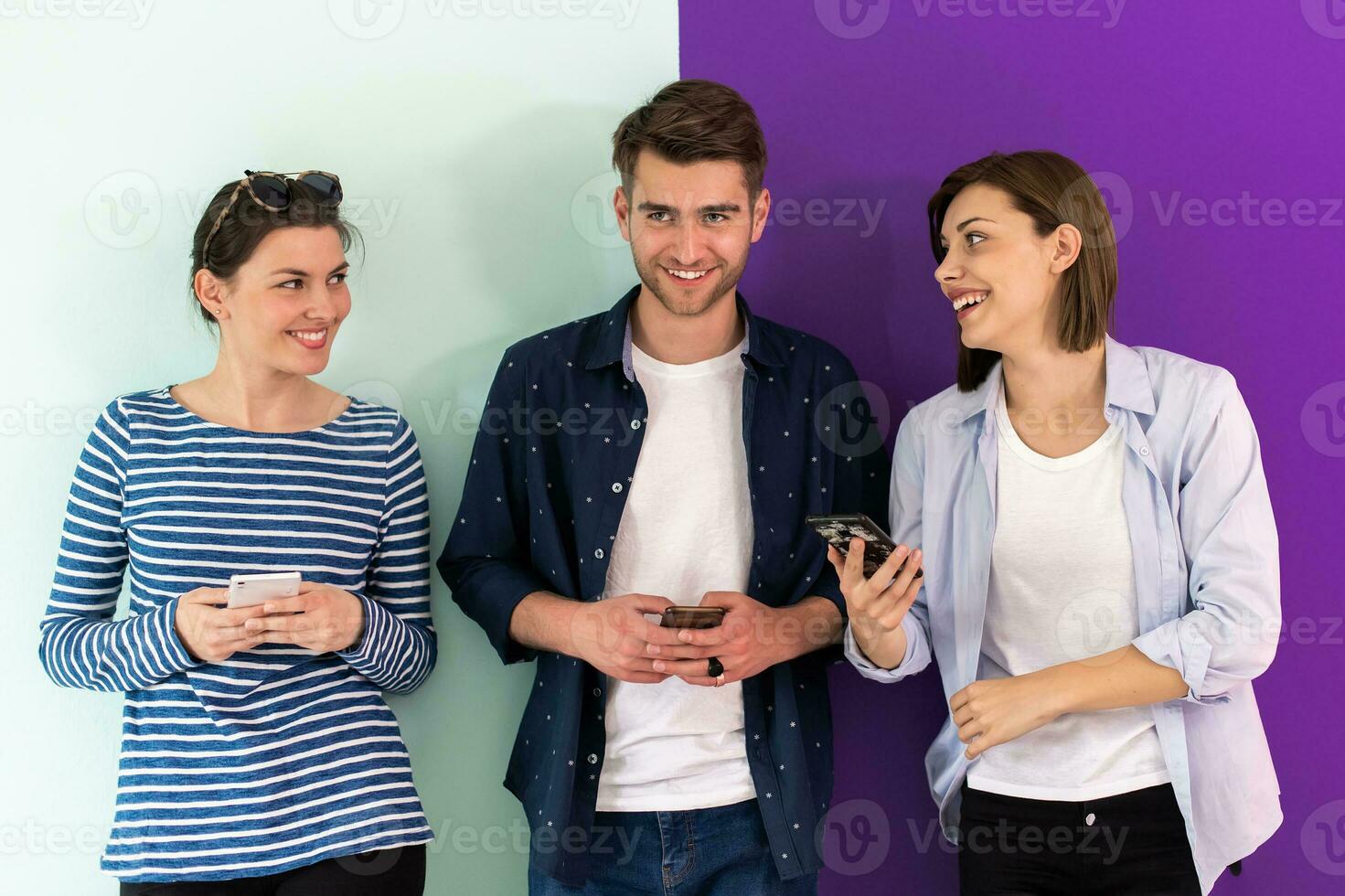 Diverse teenagers using mobile devices while posing for a studio photo in front of a colorful background