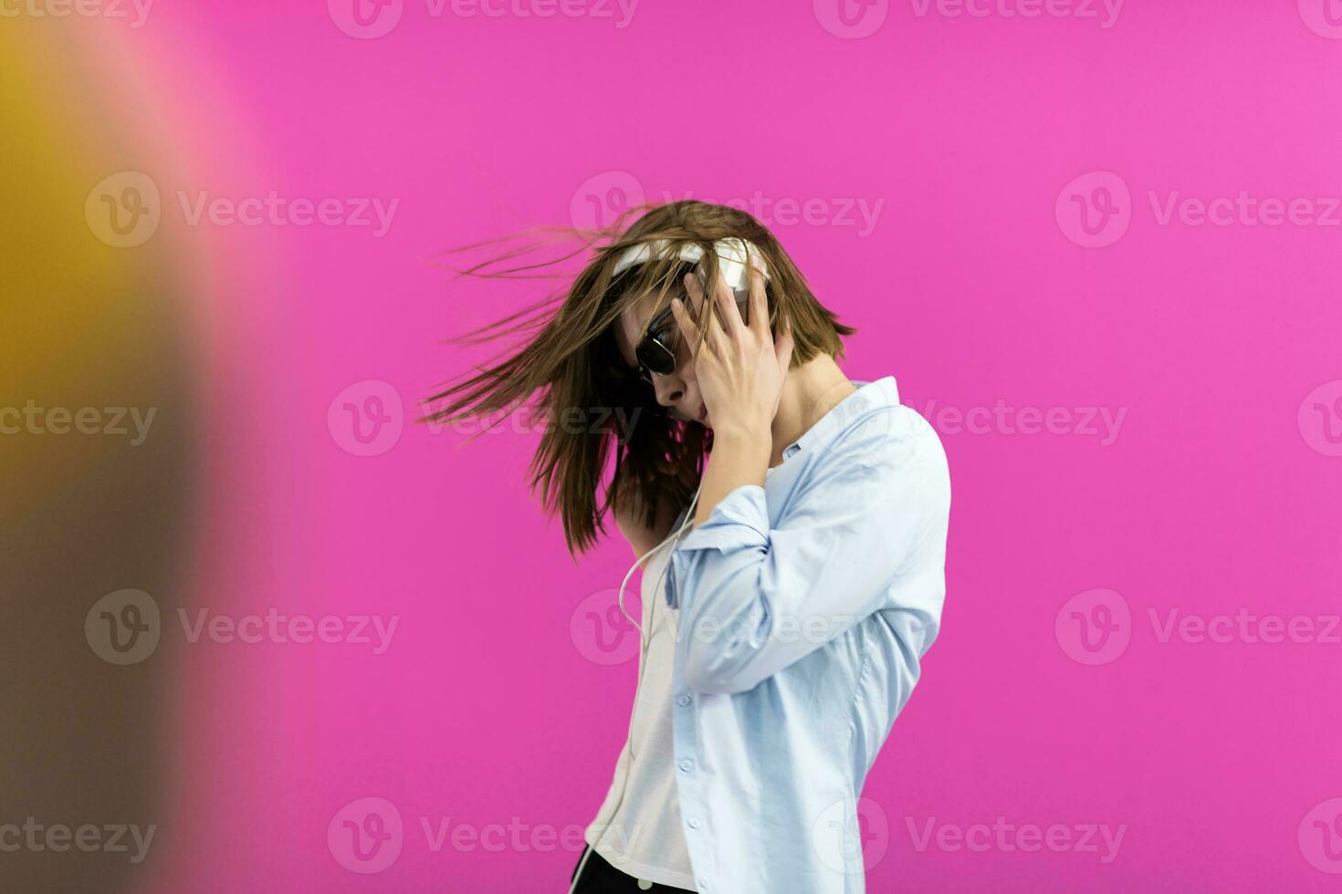 Brunette lady in black glasses dancing and listening music isolate on pink background photo