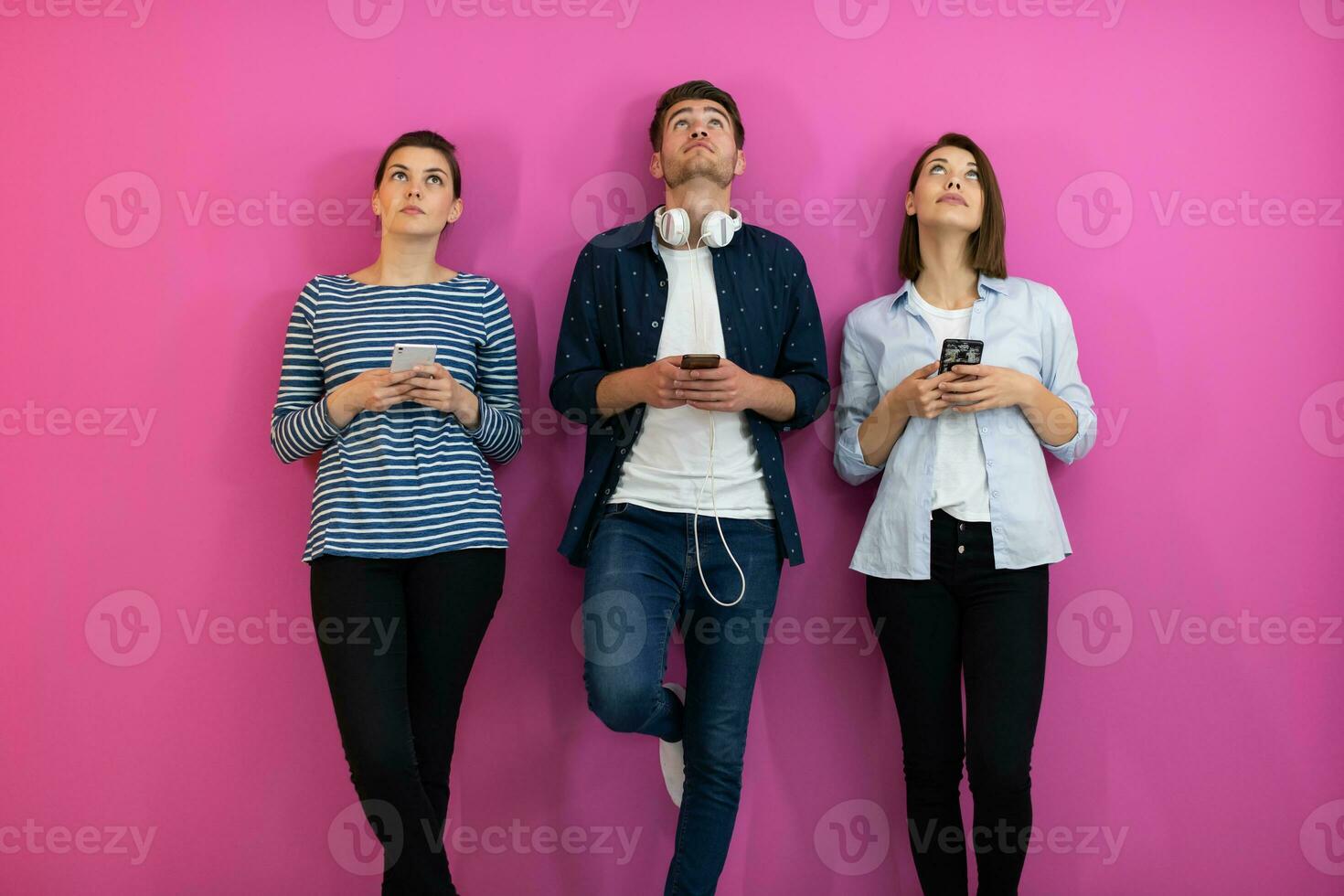 Diverse teenagers using smartphone while posing for a studio photo in front of a pink background