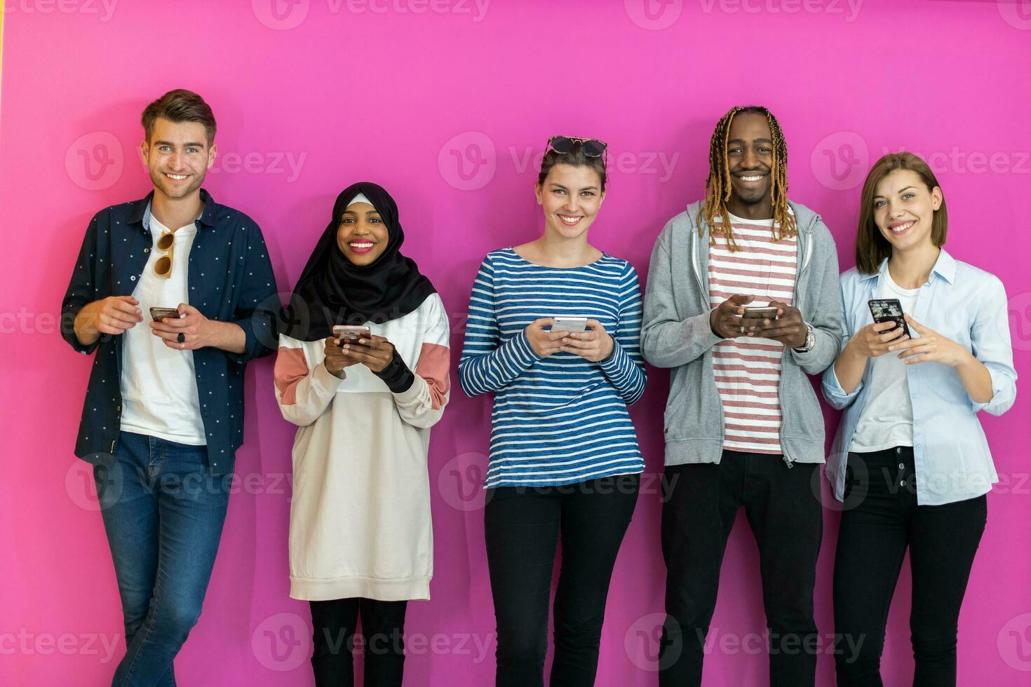 Diverse teenagers using mobile devices while posing for a studio photo in front of a colorful background