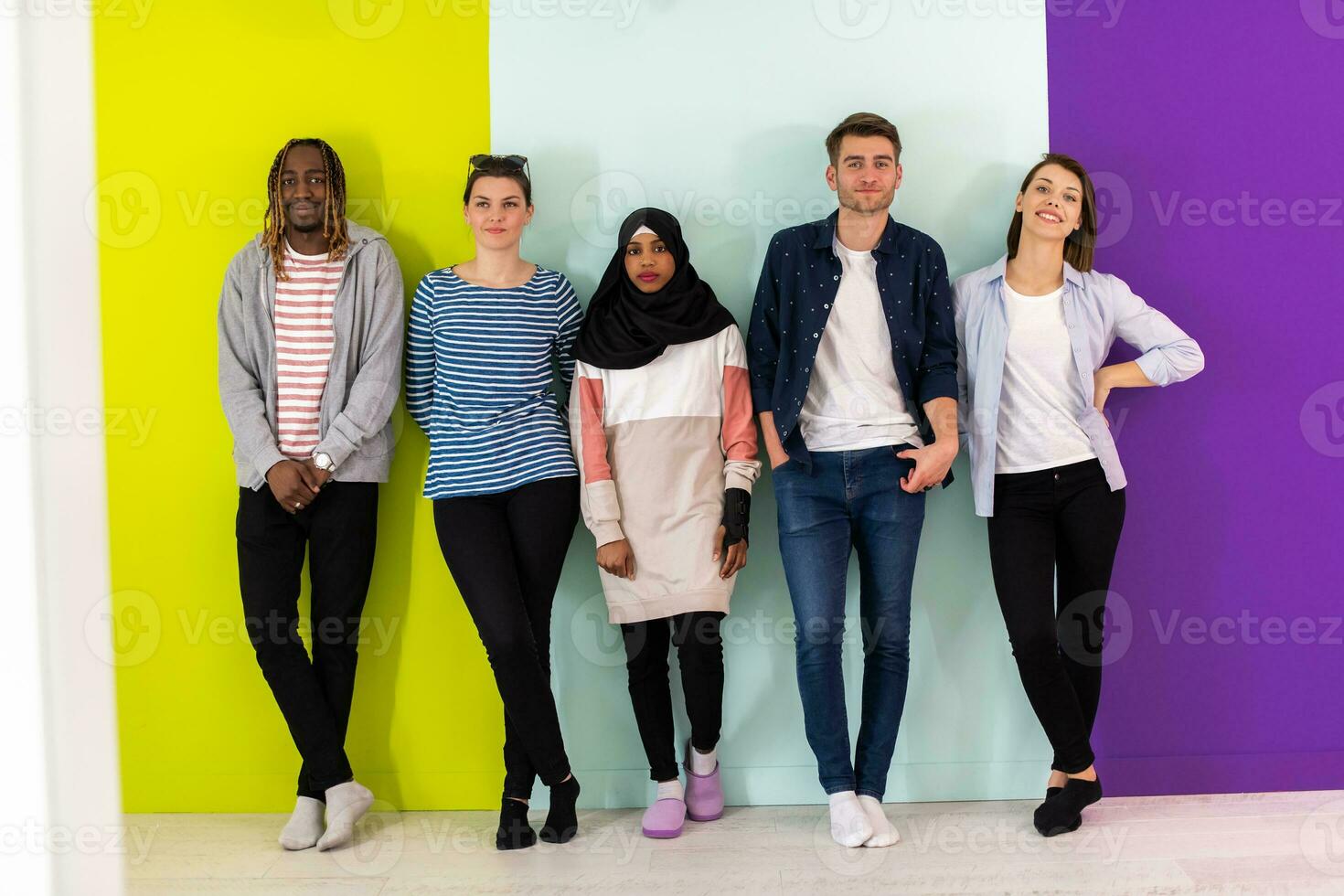 Diverse teenagers using mobile devices while posing for a studio photo in front of a colorful background