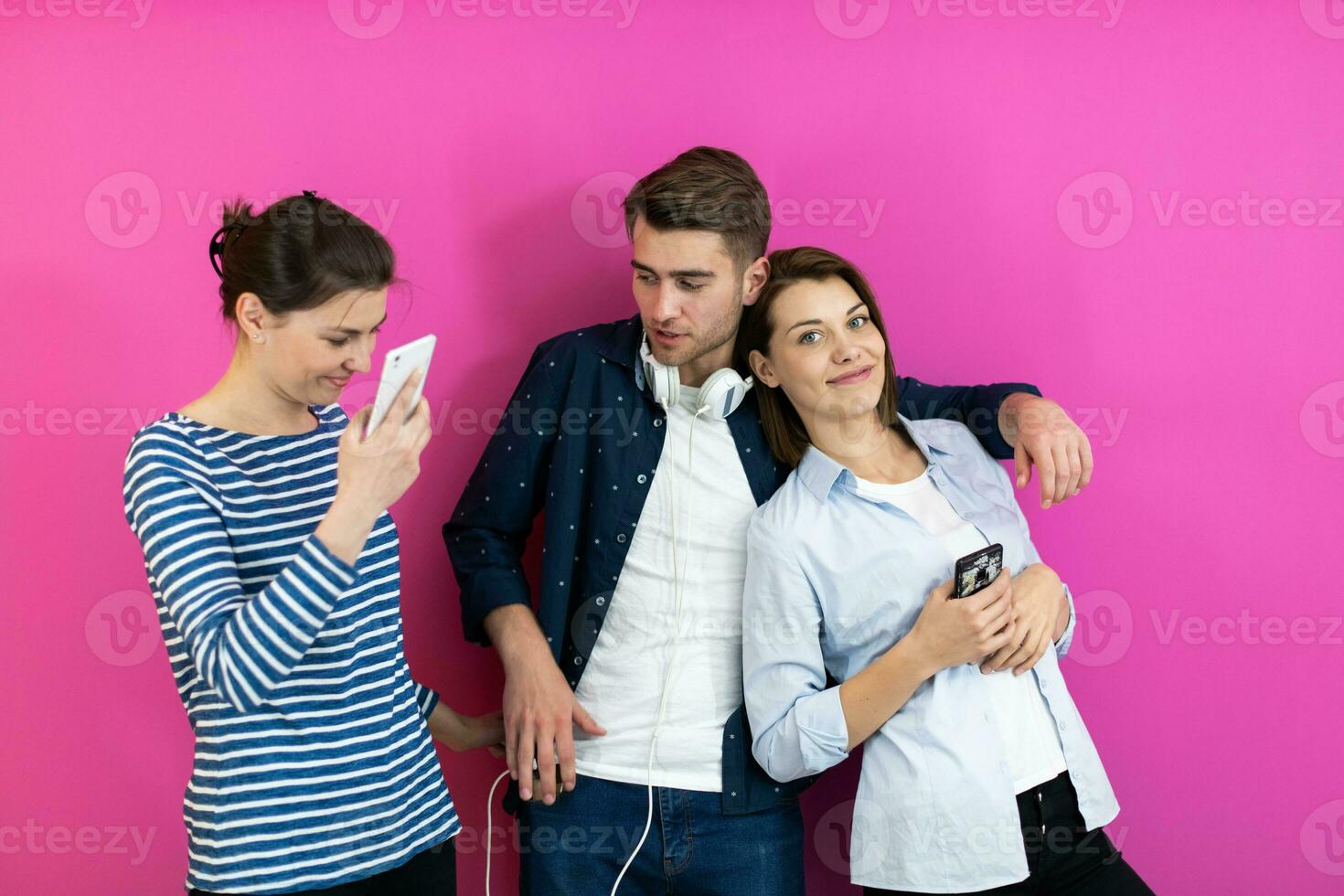 Diverse teenagers using smartphone while posing for a studio photo in front of a pink background