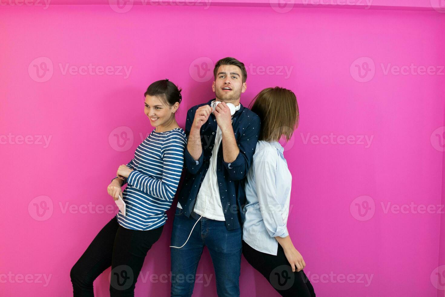 Group of young people in modern clothes posing and having fun isolated in front of pink background photo