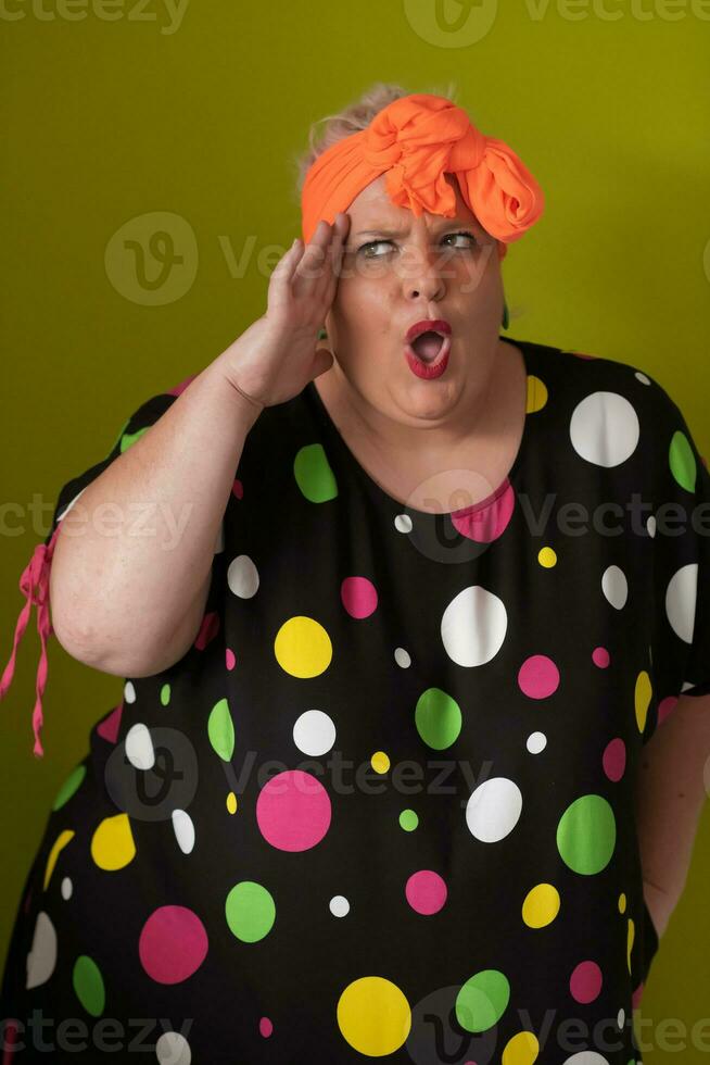 Mujer modelo sexy de talla grande con maquillaje de moda, rubia de moda con vestido corto negro posando en el fondo verde del estudio. foto