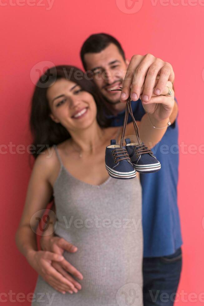 young pregnant couple holding newborn baby shoes photo