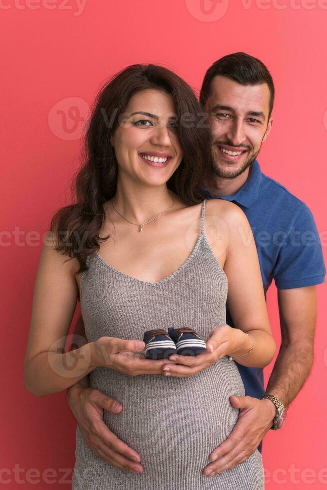 young pregnant couple holding newborn baby shoes photo
